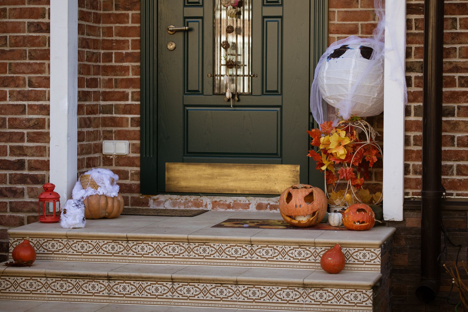 Decoración de Halloween en la puerta de casa con calabazas talladas, fantasma de tela y hojas de otoño