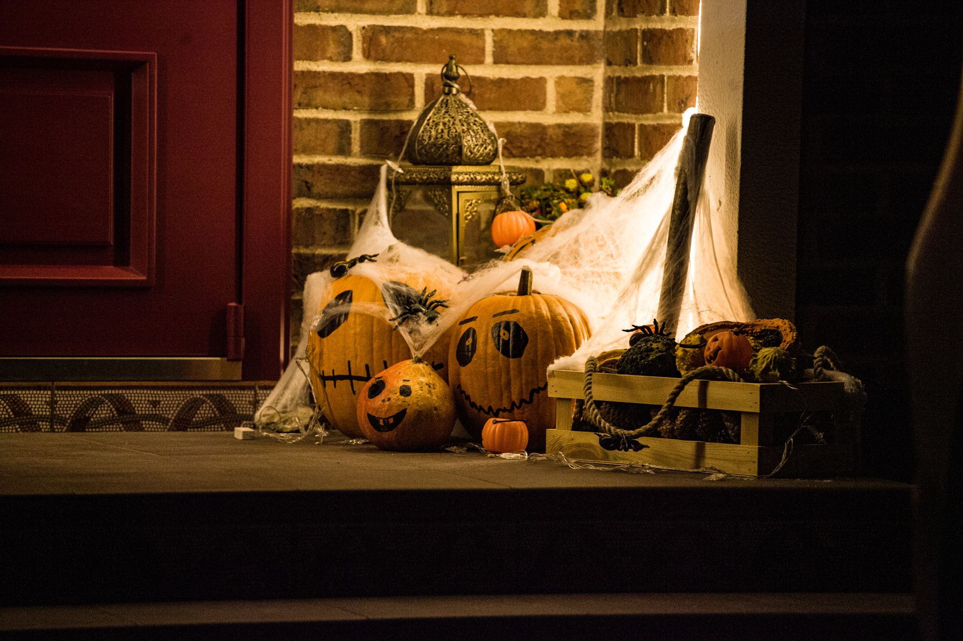 Calabazas pintadas, telarañas y farol junto a la puerta de casa como decoración de Halloween de exterior
