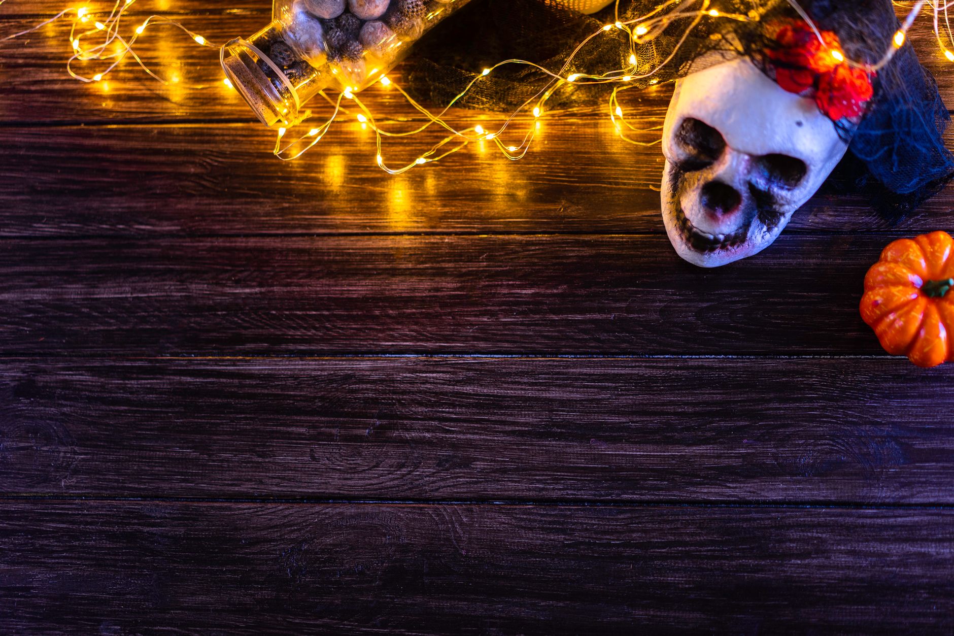 Mesa de madera decorada para Halloween con guirnalda de luces cálidas, calavera y calabaza