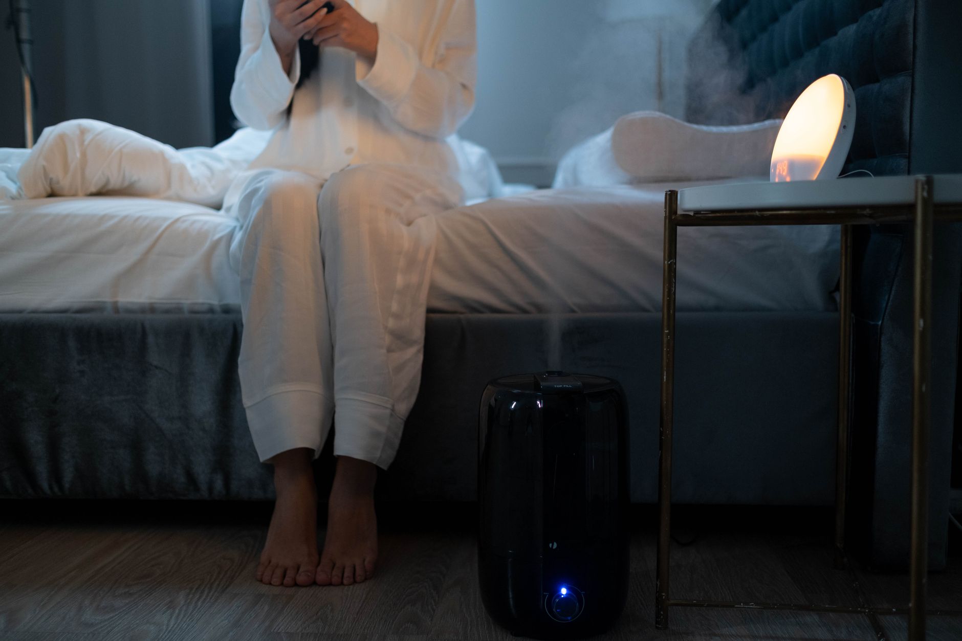 Humidificador para casa funcionando junto a la cama en un dormitorio por la noche