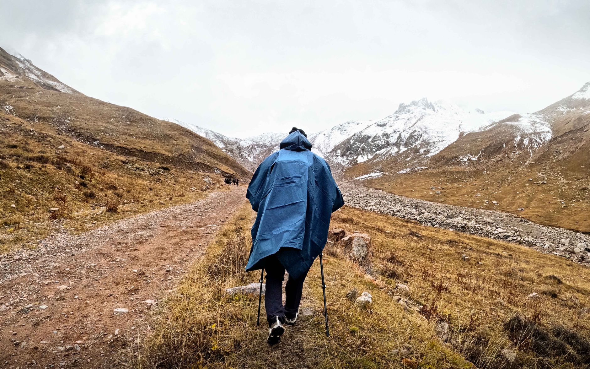 Senderista con poncho de lluvia azul cubriendo la mochila en una ruta de montaña