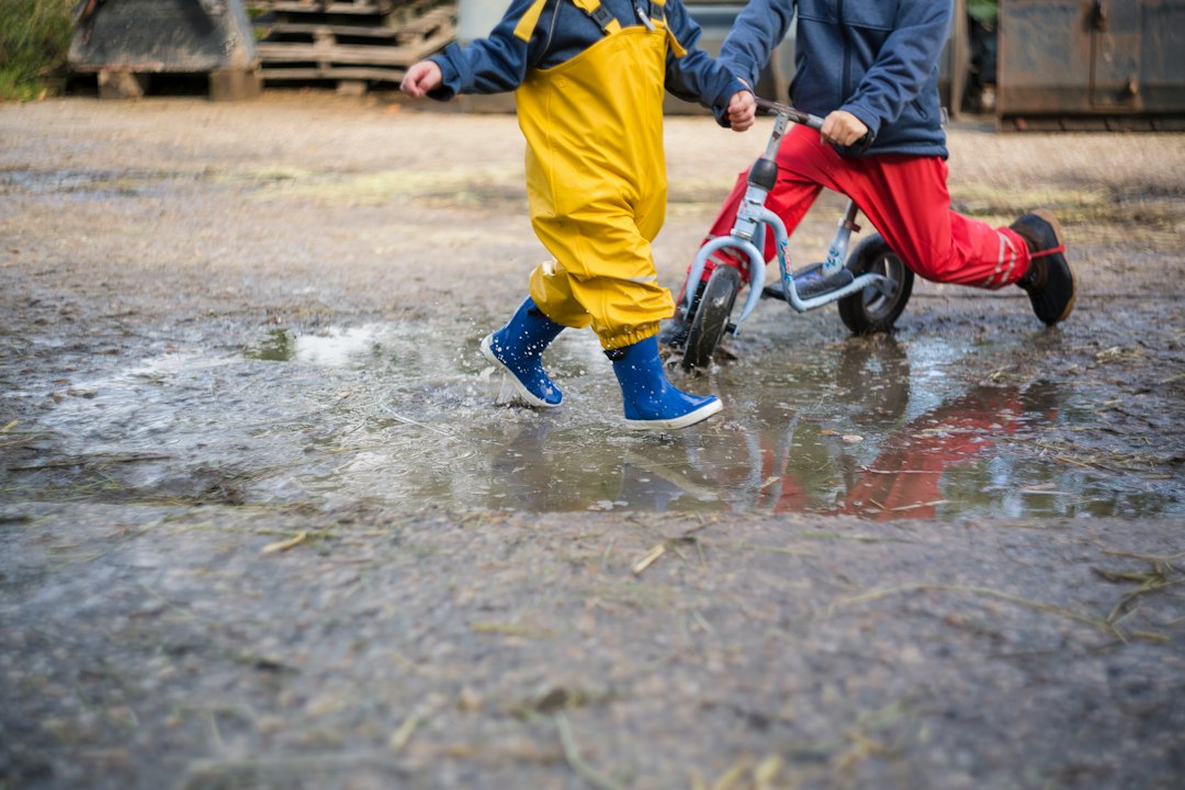Niños con pantalón impermeable y botas de agua jugando en un charco